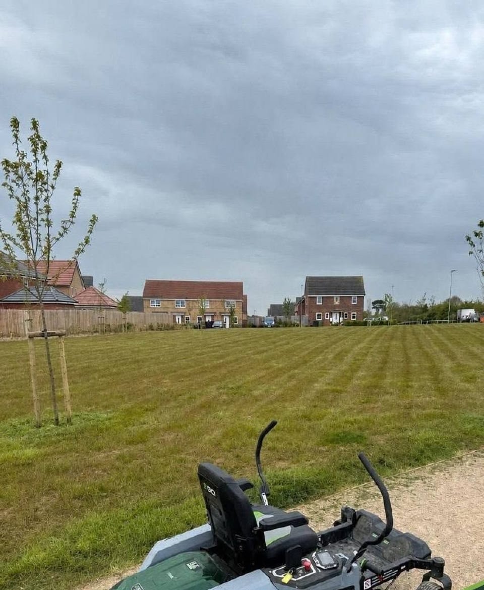 Professionally striped grass on housing-estate grounds, with a battery-powered EGO Power+ Z6 zero-turn mower on the gravel path.